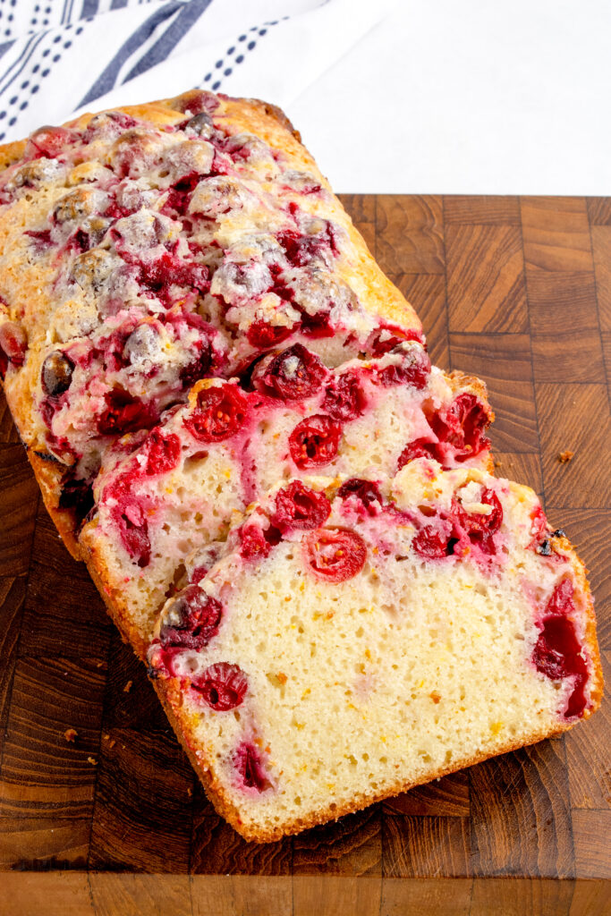 sliced loaf of cranberry bread on a wooden cutting board
