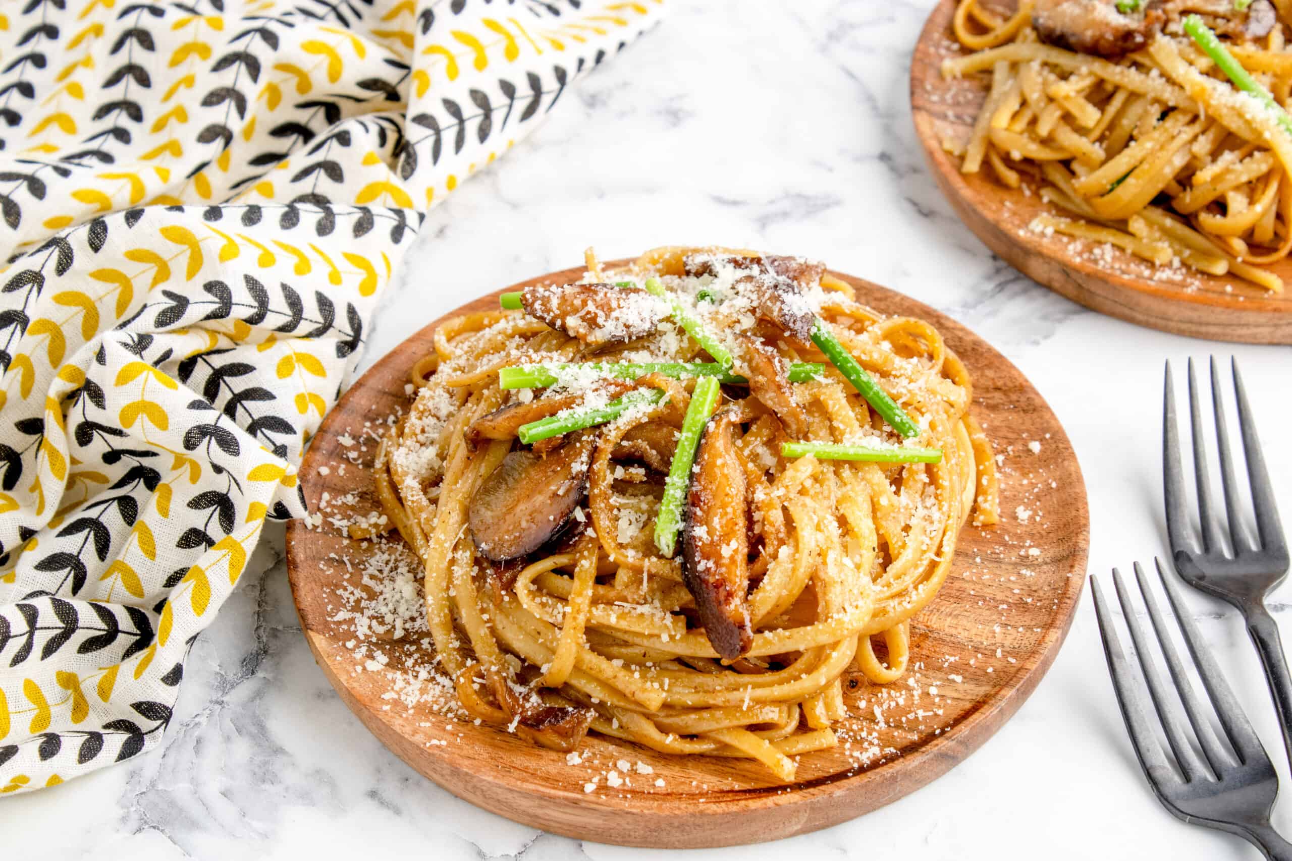 shiitake garlic noodles served on wooden plates topped with chives and grated parmesan cheese
