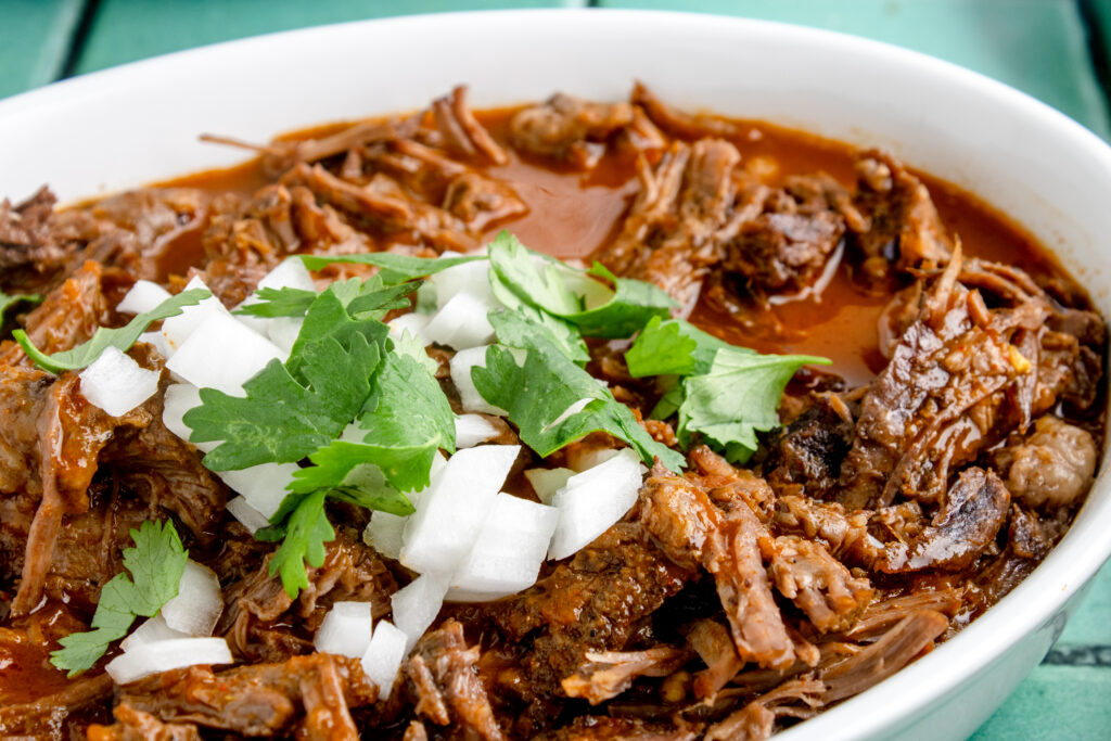 close up image of a white dish filled with birria meat topped with chopped white onions and fresh cilantro