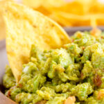 close up of guacamole in a wooden bowl with tortilla chips