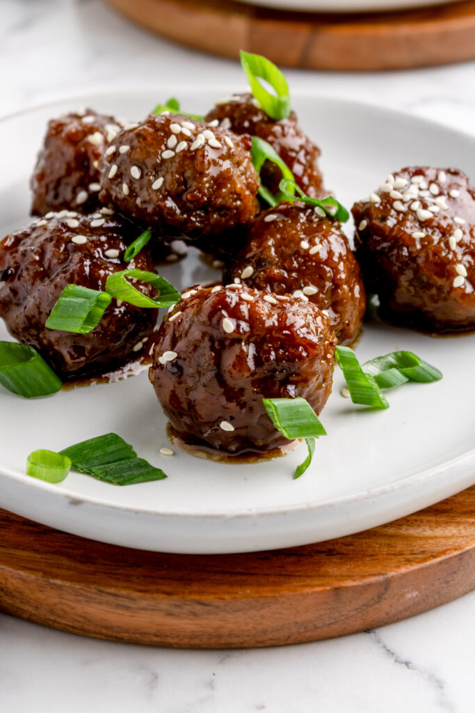 close up image of cocktail meatballs on a white plate granished with scallions and sesame seeds