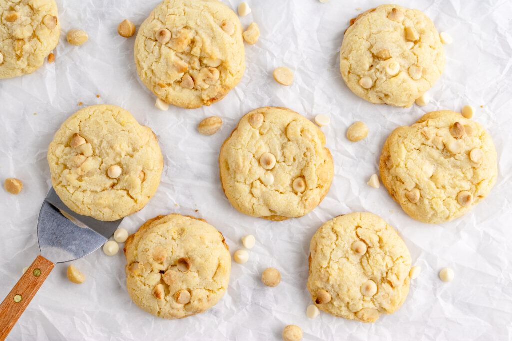 white chocolate macadamia nut cookies on crinkled parchment paper with a cookie spatula