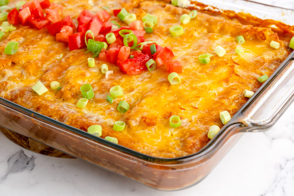 taquitos casserole in a baking dish garnished with chopped tomato and green onion